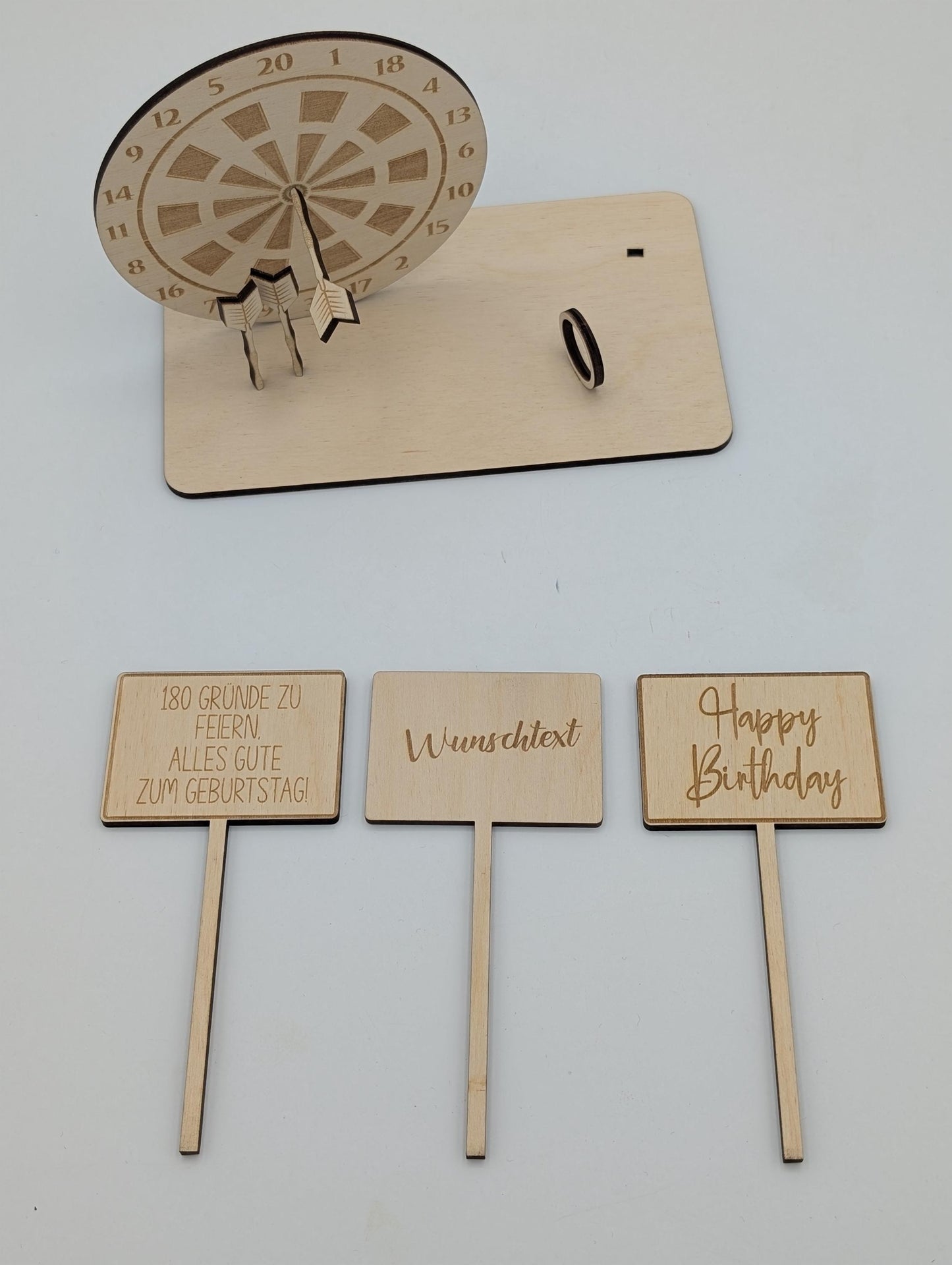 "Personalisierte Dartscheibe aus Holz mit Gravur und Geldhalter, auf einer stabilen Bodenplatte befestigt. Ein Dartpfeil steckt in der Mitte der Scheibe, kann aber auf Wunsch auf eine bestimmte Punktzahl gesetzt werden. Das gravierte Schild zeigt „Happy Birthday – 180 Gründe zu feiern“ oder eine individuelle Widmung. Perfektes Geschenk für Dartspieler zum Geburtstag, Jubiläum oder als Pokal für ein Dartturnier."