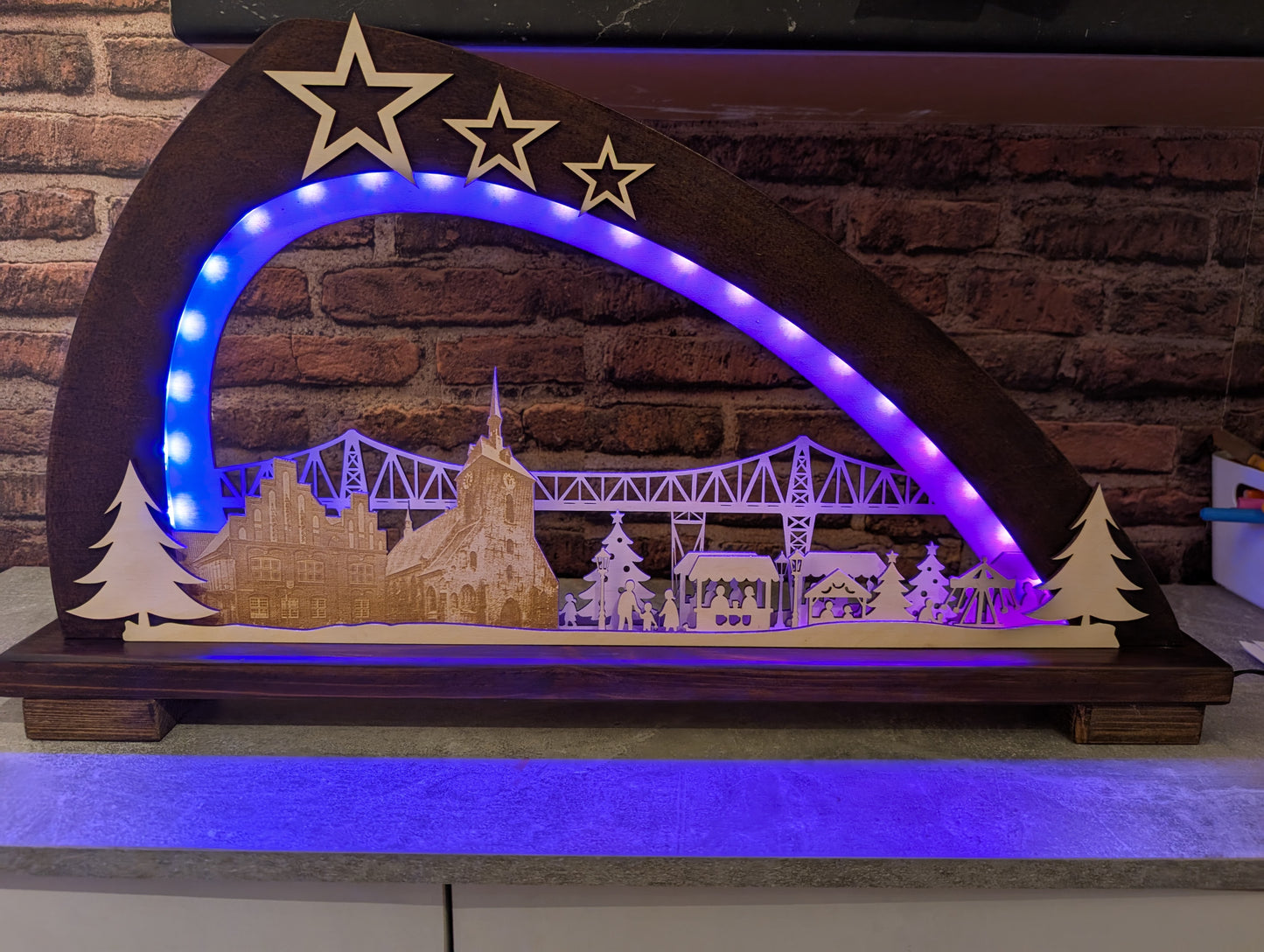 Handgefertigter Schwibbogen aus Birkenholz mit LED-Beleuchtung, zeigt Rendsburger Eisenbahnhochbrücke, Altes Rathaus, Marienkirche und Weihnachtsmarkt.