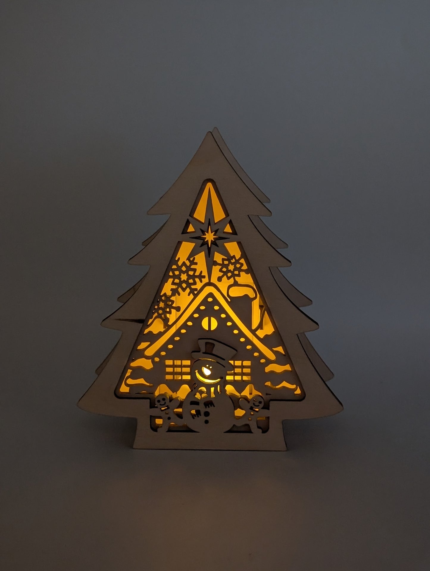 Beleuchteter Holzbaum mit Schneemann und Hausmotiv