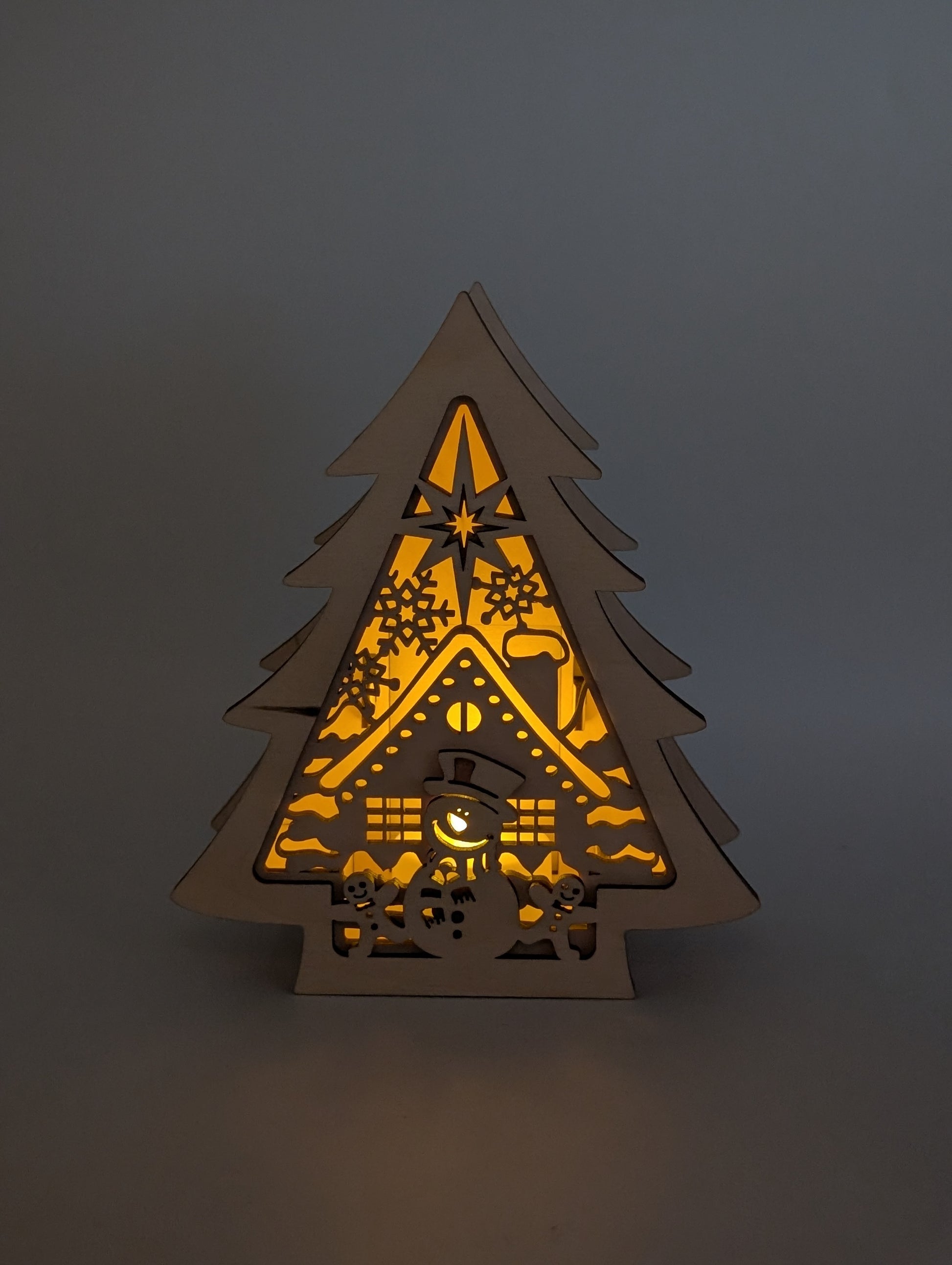 Beleuchteter Holzbaum mit Schneemann und Hausmotiv