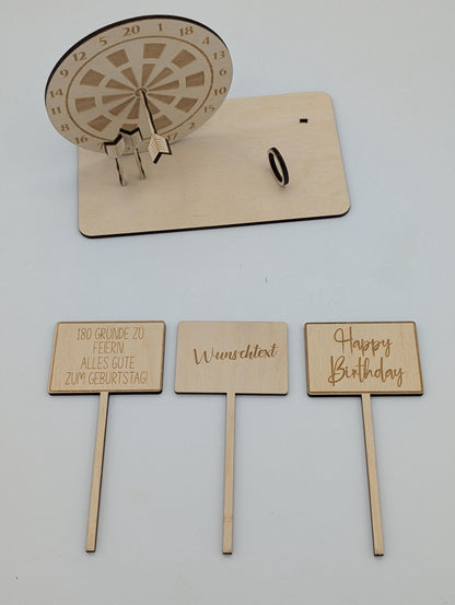 &quot;Personalisierte Dartscheibe aus Holz mit Gravur und Geldhalter, auf einer stabilen Bodenplatte befestigt. Ein Dartpfeil steckt in der Mitte der Scheibe, kann aber auf Wunsch auf eine bestimmte Punktzahl gesetzt werden. Das gravierte Schild zeigt „Happy Birthday – 180 Gründe zu feiern“ oder eine individuelle Widmung. Perfektes Geschenk für Dartspieler zum Geburtstag, Jubiläum oder als Pokal für ein Dartturnier.&quot;