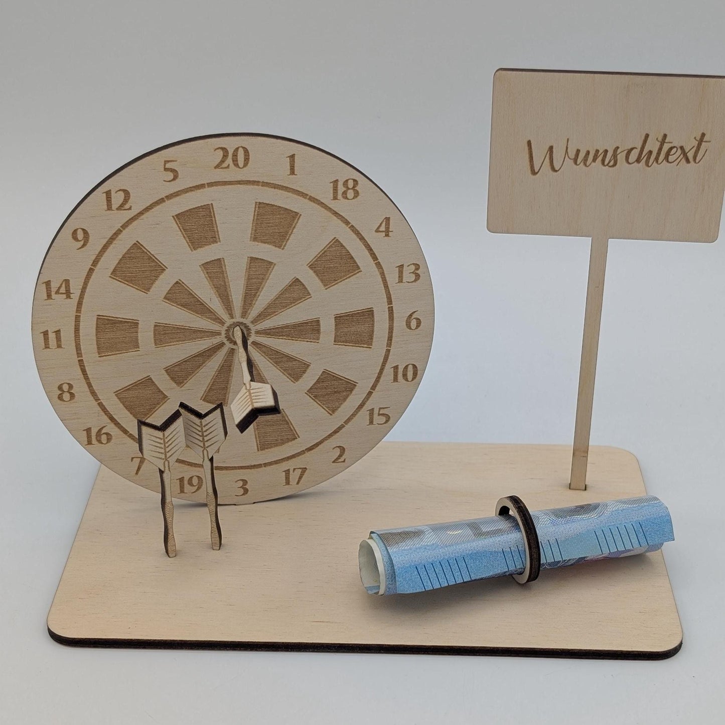 &quot;Personalisierte Dartscheibe aus Holz mit Gravur und Geldhalter, auf einer stabilen Bodenplatte befestigt. Ein Dartpfeil steckt in der Mitte der Scheibe, kann aber auf Wunsch auf eine bestimmte Punktzahl gesetzt werden. Das gravierte Schild zeigt „Happy Birthday – 180 Gründe zu feiern“ oder eine individuelle Widmung. Perfektes Geschenk für Dartspieler zum Geburtstag, Jubiläum oder als Pokal für ein Dartturnier.&quot;