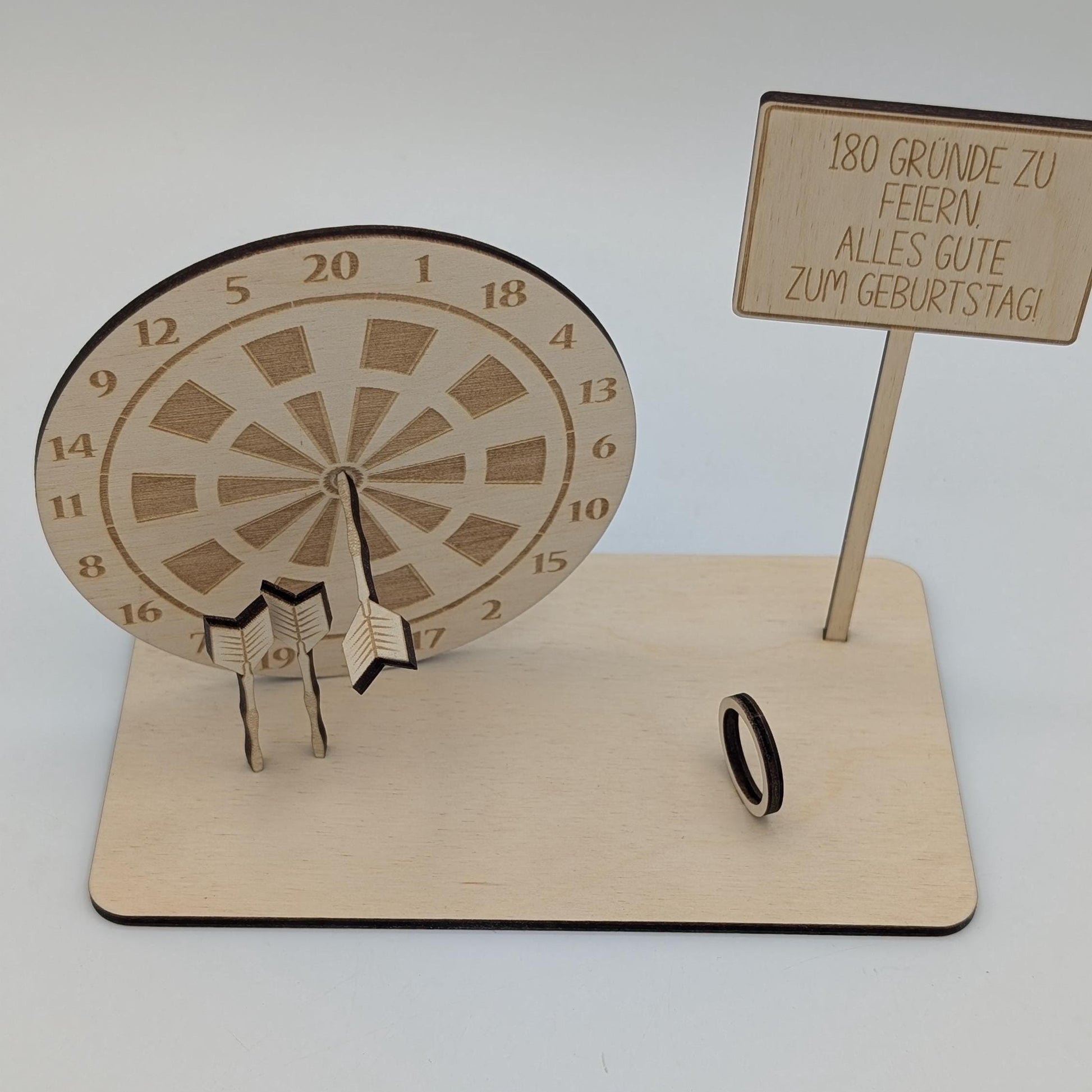 &quot;Personalisierte Dartscheibe aus Holz mit Gravur und Geldhalter, auf einer stabilen Bodenplatte befestigt. Ein Dartpfeil steckt in der Mitte der Scheibe, kann aber auf Wunsch auf eine bestimmte Punktzahl gesetzt werden. Das gravierte Schild zeigt „Happy Birthday – 180 Gründe zu feiern“ oder eine individuelle Widmung. Perfektes Geschenk für Dartspieler zum Geburtstag, Jubiläum oder als Pokal für ein Dartturnier.&quot;