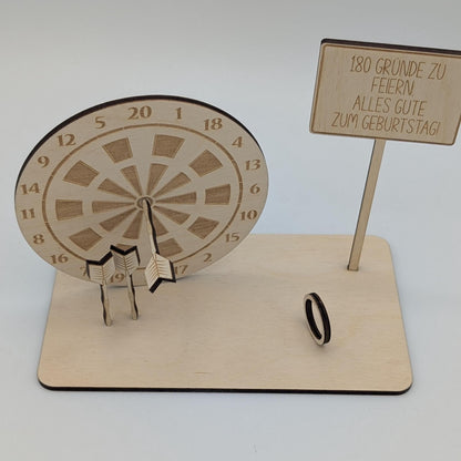 &quot;Personalisierte Dartscheibe aus Holz mit Gravur und Geldhalter, auf einer stabilen Bodenplatte befestigt. Ein Dartpfeil steckt in der Mitte der Scheibe, kann aber auf Wunsch auf eine bestimmte Punktzahl gesetzt werden. Das gravierte Schild zeigt „Happy Birthday – 180 Gründe zu feiern“ oder eine individuelle Widmung. Perfektes Geschenk für Dartspieler zum Geburtstag, Jubiläum oder als Pokal für ein Dartturnier.&quot;